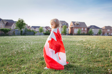 Criança envolta na bandeira do Canadá em um campo verde
