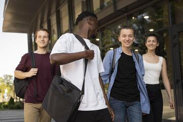 Grupo de estudantes caminhando juntos em frente a um edifício moderno, sorrindo e interagindo
