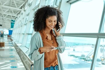 Mulher sorridente usando celular e segurando um cartão em um aeroporto
